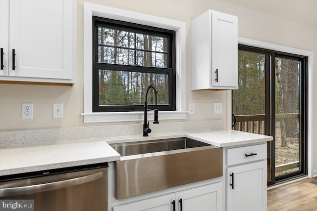 kitchen with stainless steel dishwasher, a sink, white cabinetry, and light stone countertops