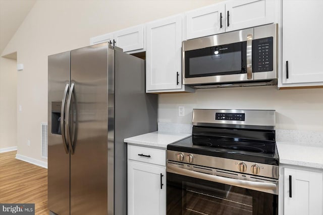 kitchen with appliances with stainless steel finishes, white cabinets, light wood-style floors, and baseboards