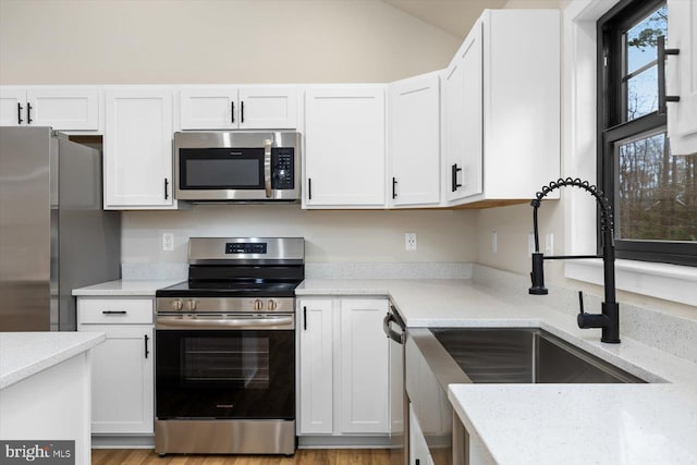 kitchen featuring white cabinets, light wood-type flooring, stainless steel appliances, and a sink