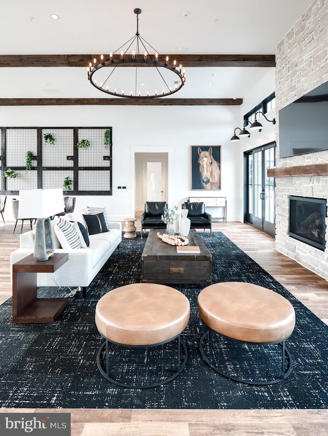 living area with a large fireplace, wood finished floors, beam ceiling, and an inviting chandelier