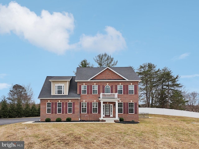 colonial inspired home featuring a front lawn, fence, and brick siding