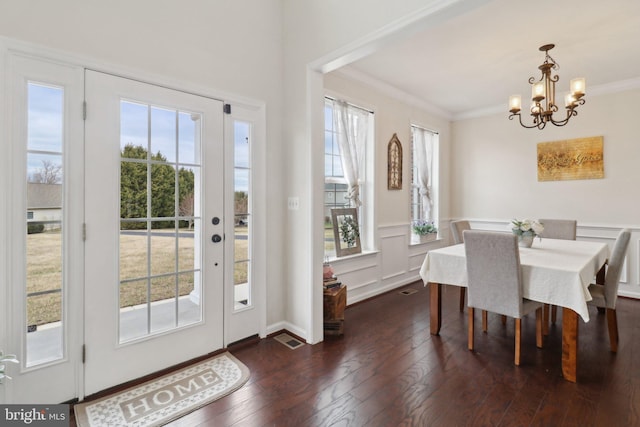 dining room featuring a decorative wall, a wainscoted wall, dark wood-type flooring, ornamental molding, and an inviting chandelier