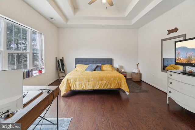 bedroom featuring a tray ceiling, visible vents, multiple windows, and wood finished floors