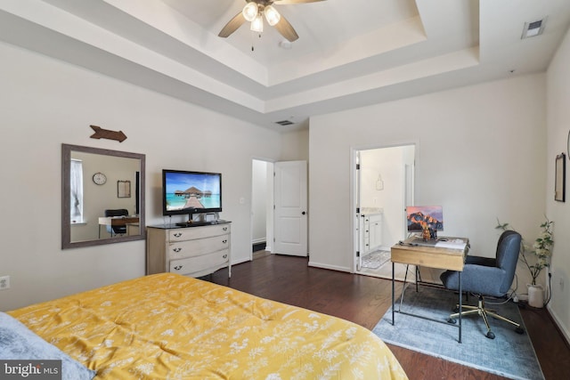 bedroom featuring dark wood-style floors, a raised ceiling, visible vents, and connected bathroom