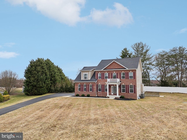 colonial home featuring brick siding, fence, a balcony, and a front lawn