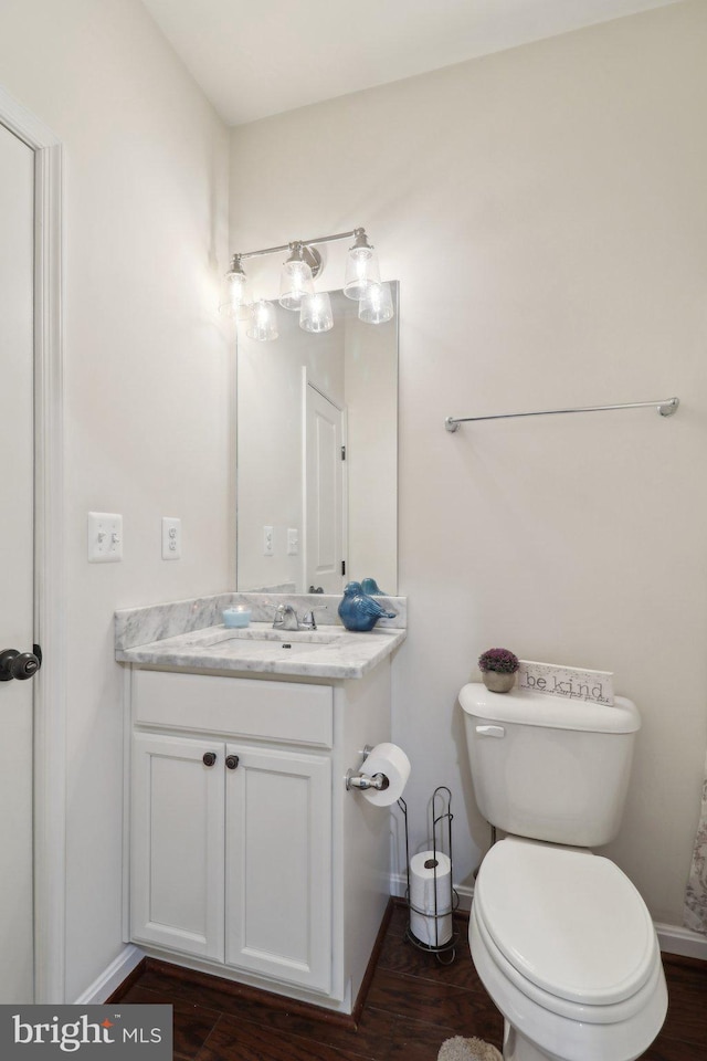 half bath with toilet, baseboards, wood finished floors, and vanity