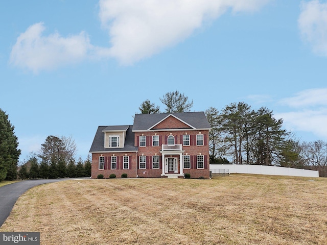 colonial home featuring a front lawn, fence, and brick siding