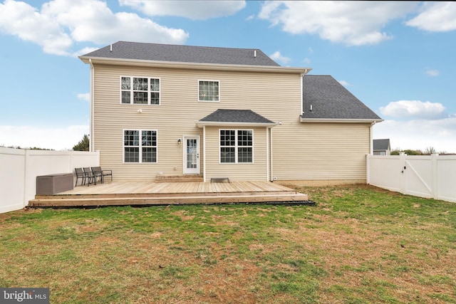 back of property with a deck, a fenced backyard, a yard, roof with shingles, and a gate