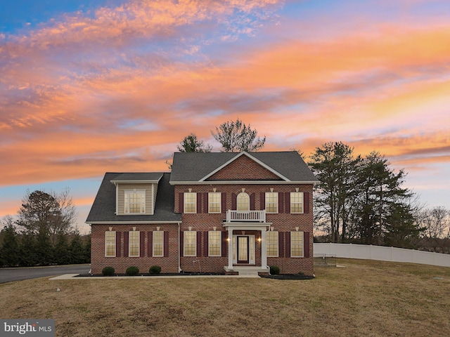 georgian-style home with a front yard, brick siding, and fence