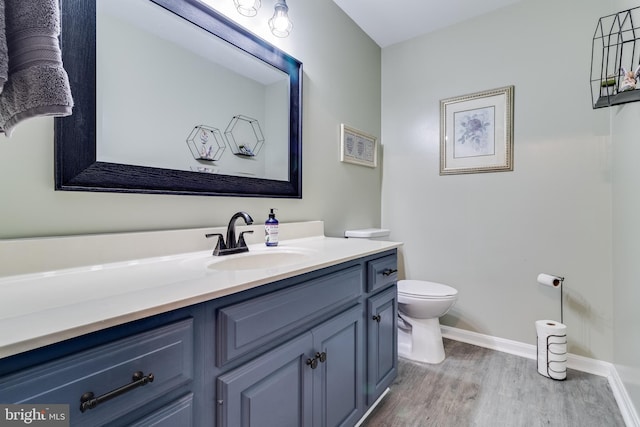 half bathroom featuring toilet, baseboards, wood finished floors, and vanity