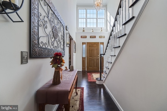 foyer entrance featuring baseboards, a towering ceiling, dark wood-style floors, stairs, and a notable chandelier