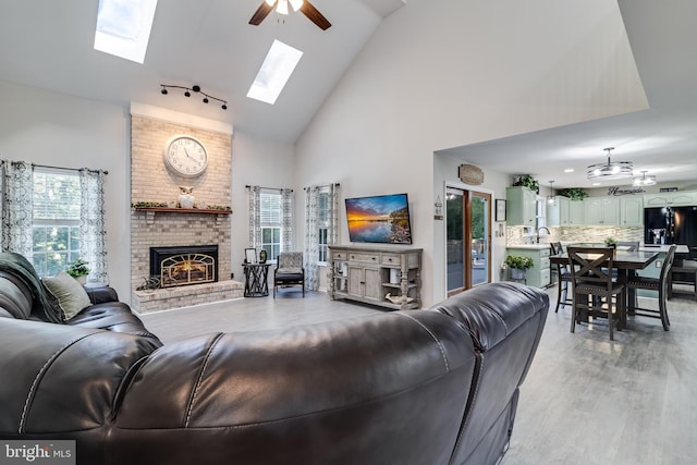 living area with ceiling fan, high vaulted ceiling, a fireplace, and light wood-style flooring