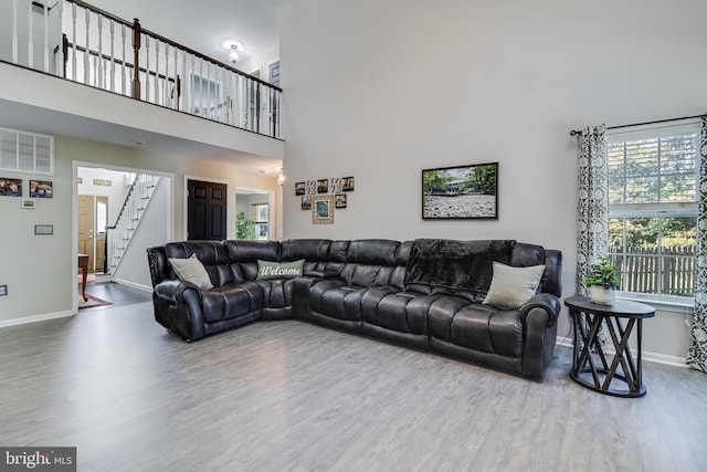 living room featuring wood finished floors, visible vents, a towering ceiling, baseboards, and stairway