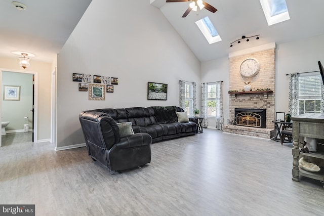 living area with a fireplace, ceiling fan, wood finished floors, high vaulted ceiling, and baseboards