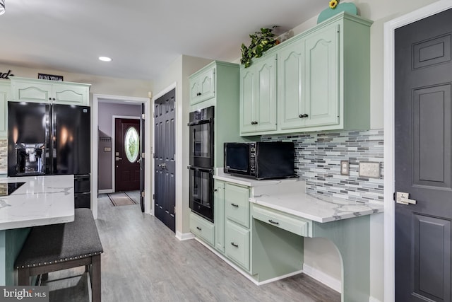 kitchen featuring light stone countertops, black appliances, light wood finished floors, and backsplash