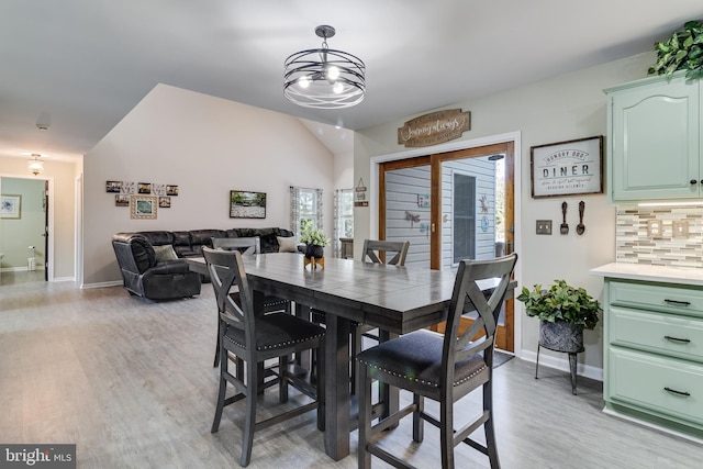 dining room featuring vaulted ceiling, light wood-type flooring, a notable chandelier, and baseboards