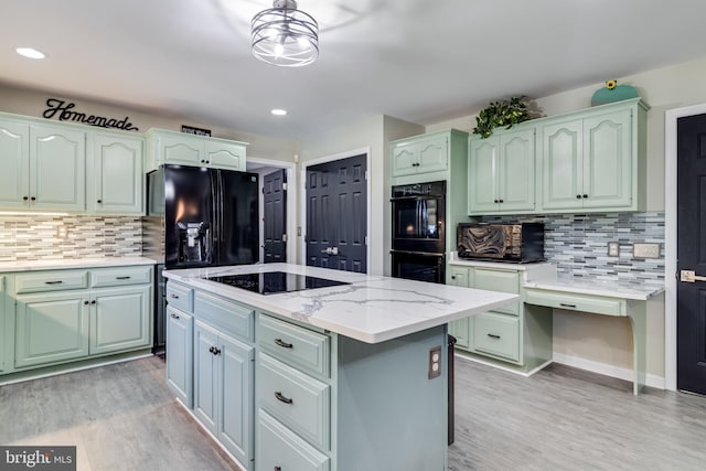 kitchen featuring light stone counters, light wood-style flooring, a center island, black appliances, and tasteful backsplash