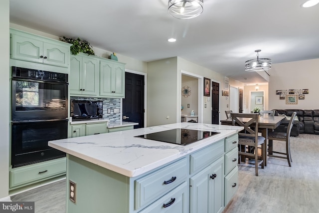 kitchen with light stone counters, light wood finished floors, open floor plan, a kitchen island, and black appliances