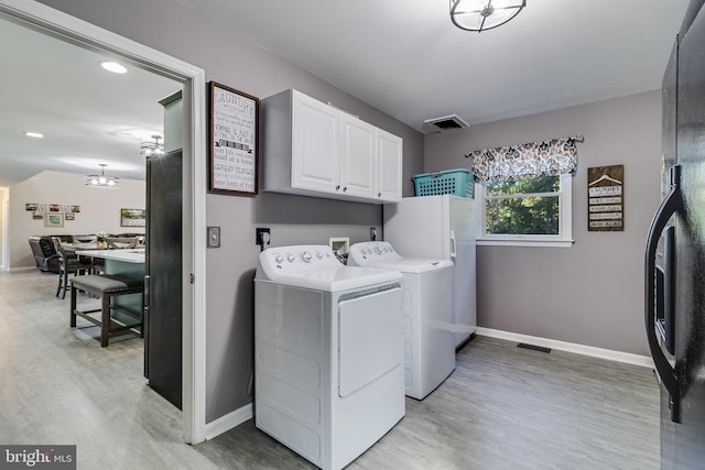 clothes washing area featuring separate washer and dryer, light wood-style flooring, cabinet space, and baseboards