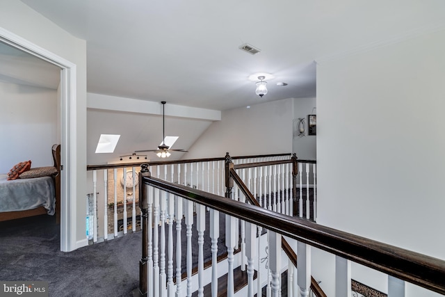 corridor with vaulted ceiling with skylight, carpet, visible vents, and an upstairs landing