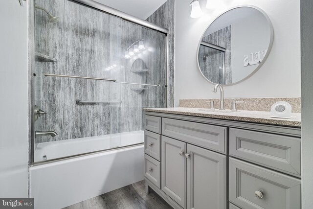 bathroom with bath / shower combo with glass door, wood finished floors, and vanity