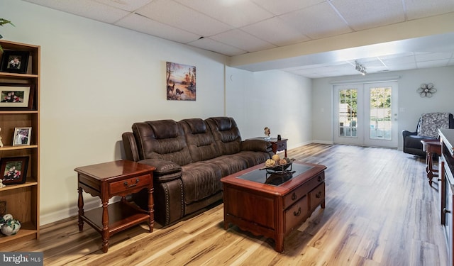 living room with light wood-style floors, french doors, a drop ceiling, and baseboards