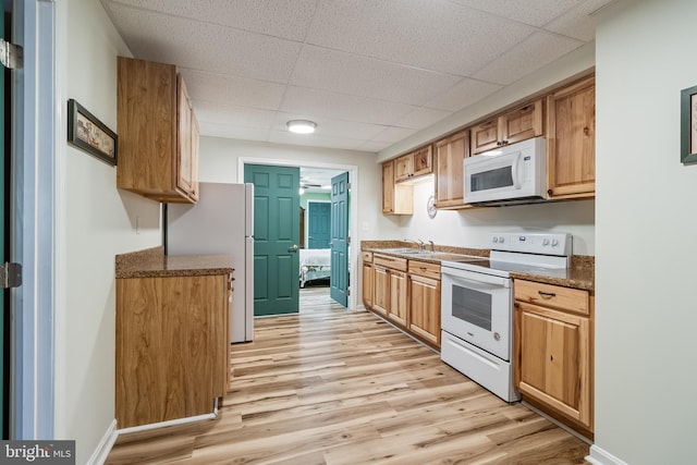 kitchen with a paneled ceiling, light wood-style floors, a sink, white appliances, and baseboards