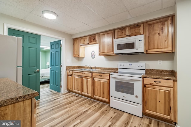 kitchen with white appliances, dark countertops, a paneled ceiling, light wood-style floors, and a sink