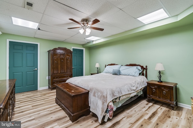 bedroom with light wood finished floors, baseboards, visible vents, a drop ceiling, and ceiling fan