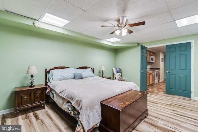 bedroom featuring ceiling fan, light wood-type flooring, a paneled ceiling, and baseboards