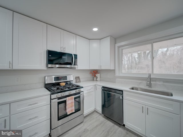 kitchen with recessed lighting, appliances with stainless steel finishes, white cabinets, a sink, and light wood-type flooring