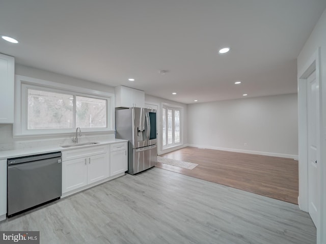 kitchen with white cabinets, light wood-style flooring, appliances with stainless steel finishes, light countertops, and a sink