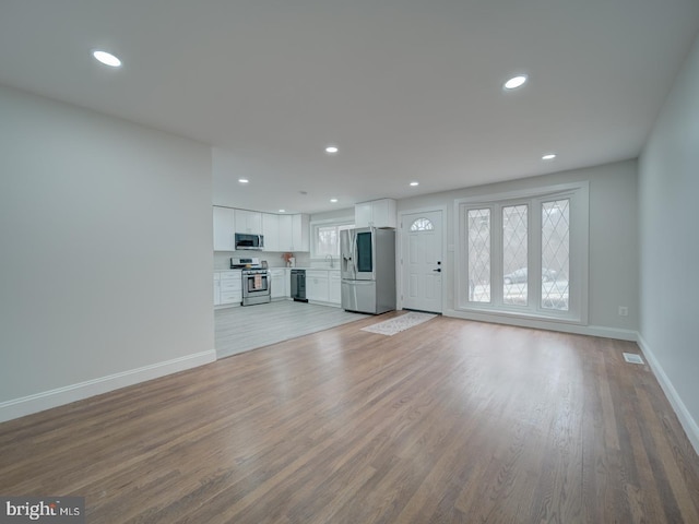 unfurnished living room with recessed lighting, light wood-type flooring, and baseboards