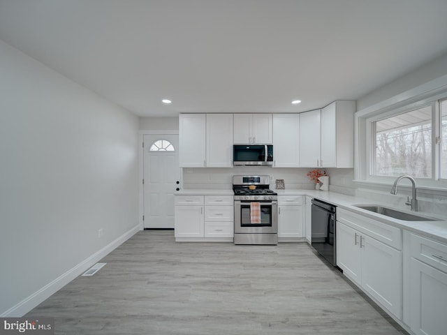 kitchen with appliances with stainless steel finishes, a sink, white cabinetry, and a healthy amount of sunlight