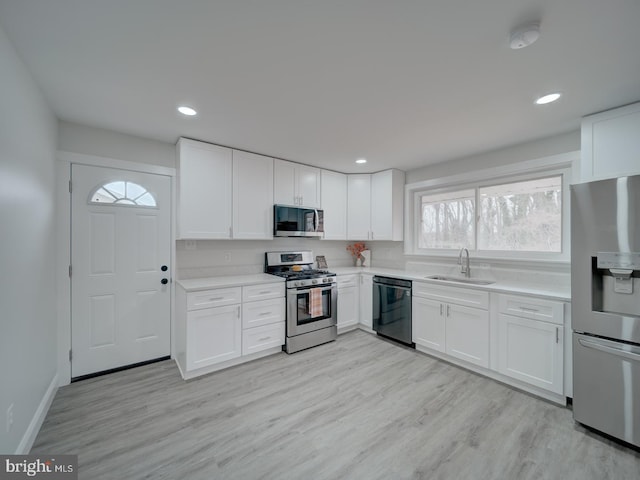 kitchen featuring light countertops, light wood-style flooring, appliances with stainless steel finishes, white cabinets, and a sink