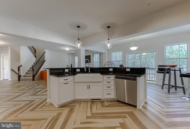 kitchen featuring a kitchen island with sink, a sink, white cabinets, stainless steel dishwasher, and decorative light fixtures