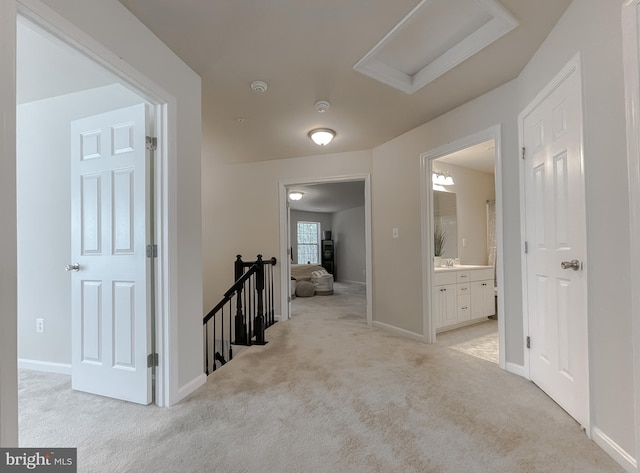 hallway with light carpet, an upstairs landing, attic access, and baseboards