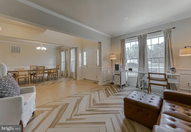 living room featuring visible vents, crown molding, a chandelier, a wainscoted wall, and a decorative wall