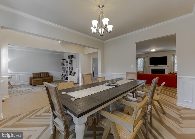 dining room featuring wainscoting, a fireplace, an inviting chandelier, and ornamental molding