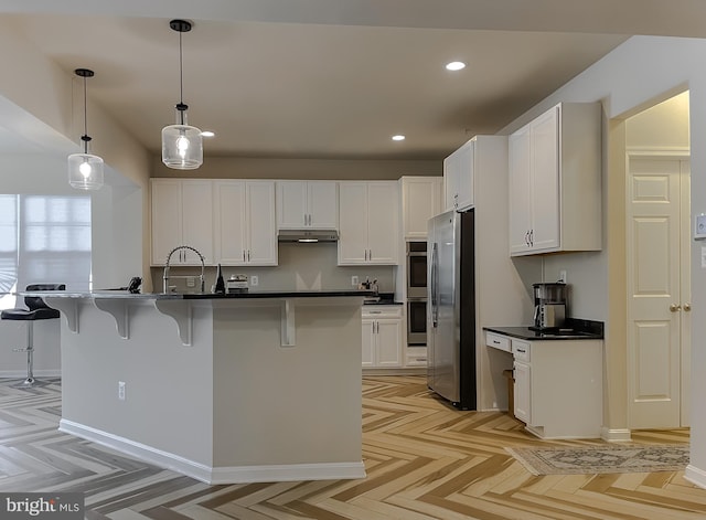 kitchen featuring under cabinet range hood, recessed lighting, appliances with stainless steel finishes, a kitchen breakfast bar, and white cabinetry