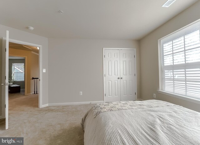 bedroom with multiple windows, light colored carpet, visible vents, and a closet