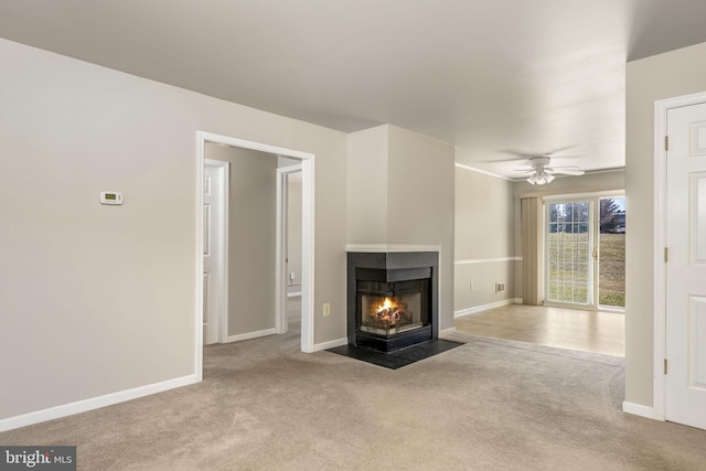 unfurnished living room featuring a multi sided fireplace, ceiling fan, baseboards, and carpet