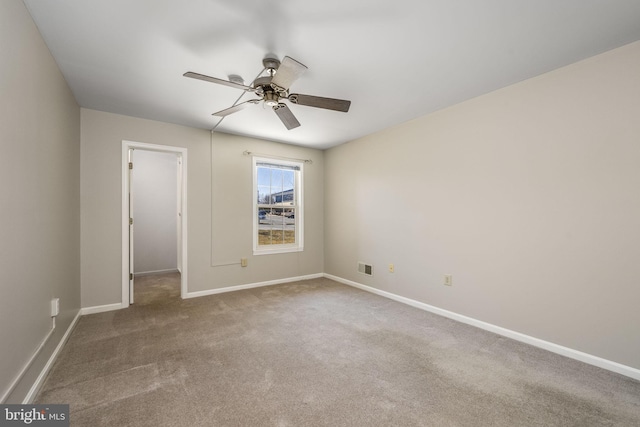 carpeted spare room with visible vents, baseboards, and ceiling fan