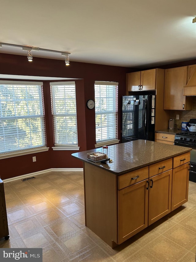 kitchen featuring refrigerator, a center island, visible vents, black gas range oven, and dark stone counters