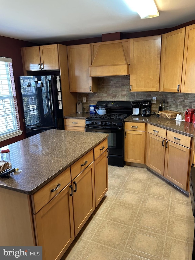 kitchen with black gas stove, fridge, backsplash, dark stone counters, and custom range hood