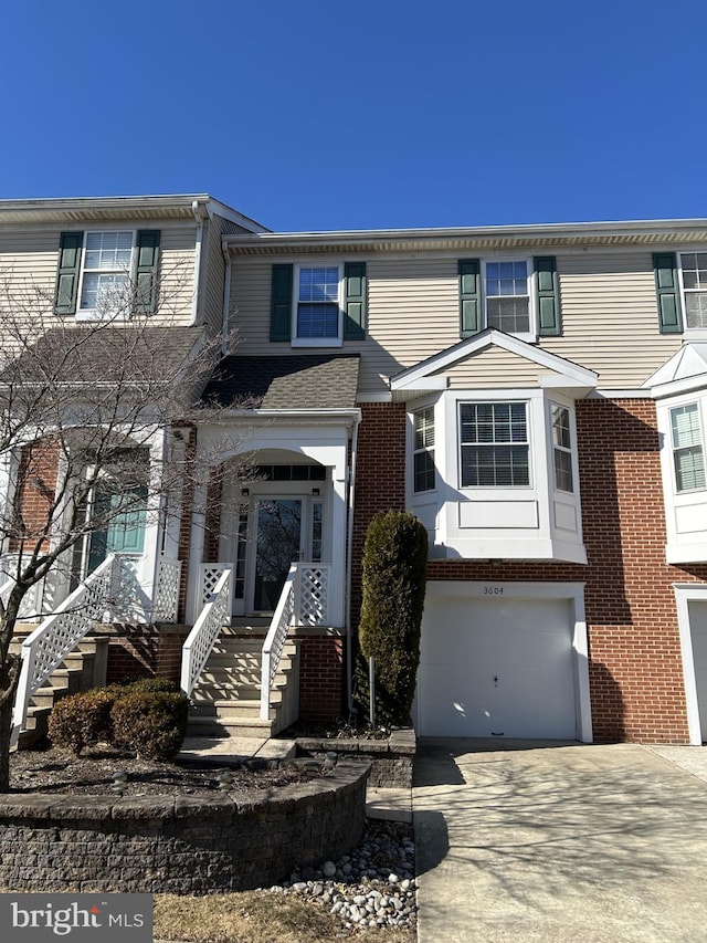 multi unit property featuring a garage, stairs, concrete driveway, and brick siding