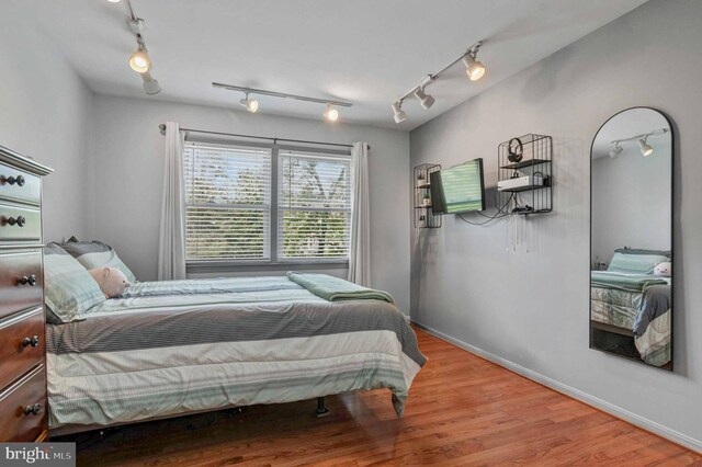 bedroom featuring wood finished floors, rail lighting, and baseboards