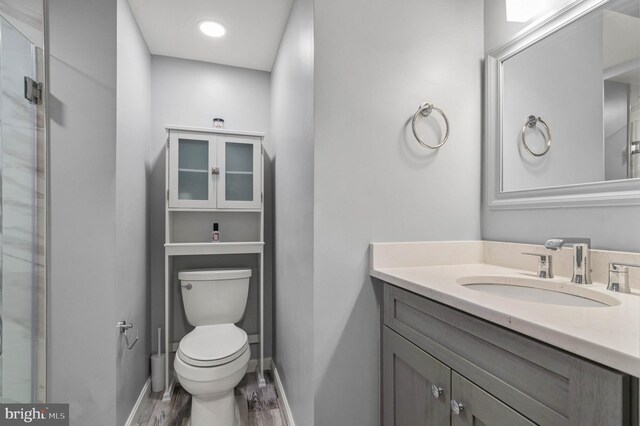 full bath with wood finished floors, a shower with door, vanity, baseboards, and toilet