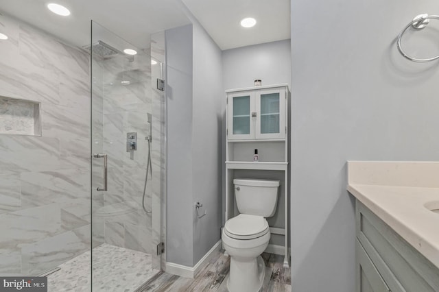 bathroom featuring wood finished floors, a marble finish shower, vanity, baseboards, and toilet