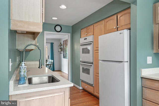 kitchen featuring light wood finished floors, a sink, recessed lighting, white appliances, and light countertops